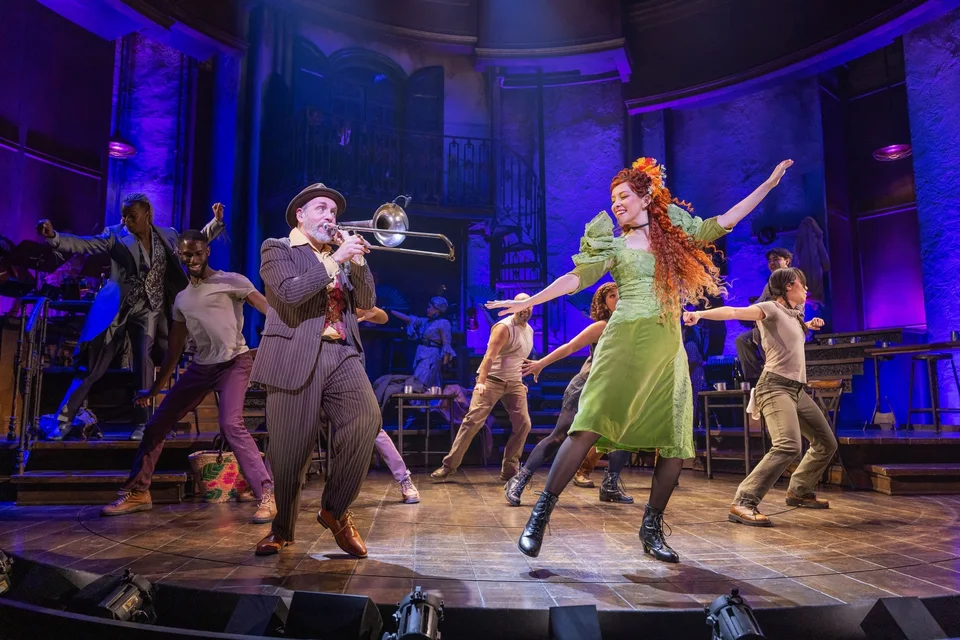 Hadestown ensemble performing under coloured stage lights