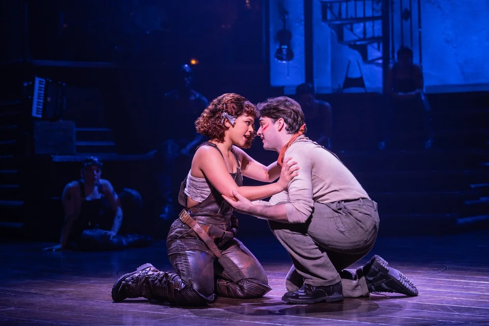 Two Hadestown performers kneeling together on stage