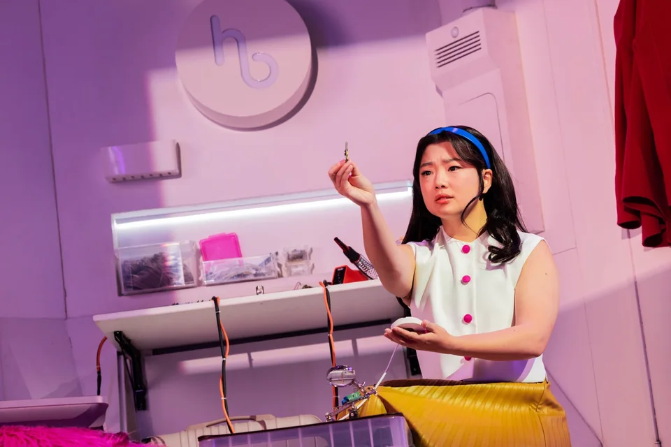 A Maybe Happy Ending performer beside a desk on a pink set