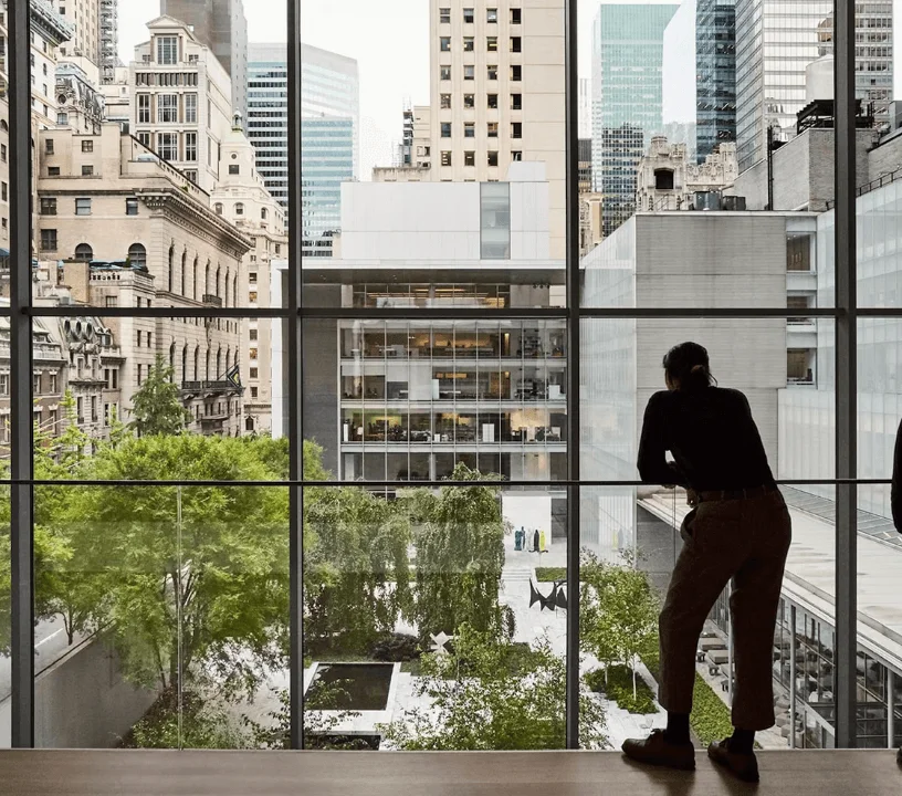 Visitor looking through a large museum window towards Midtown buildings