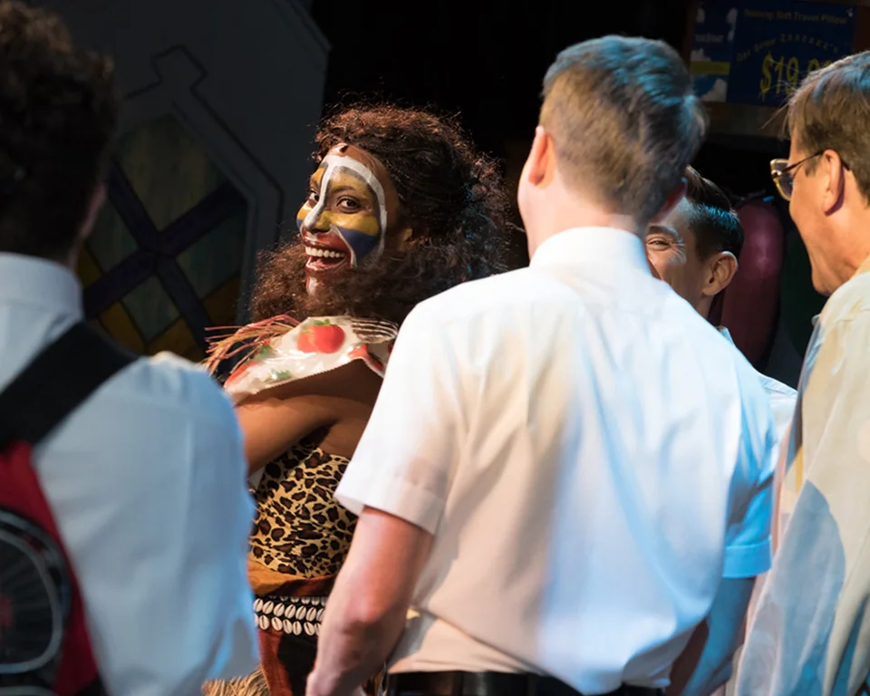 The Book of Mormon performers interacting in a colourful stage scene