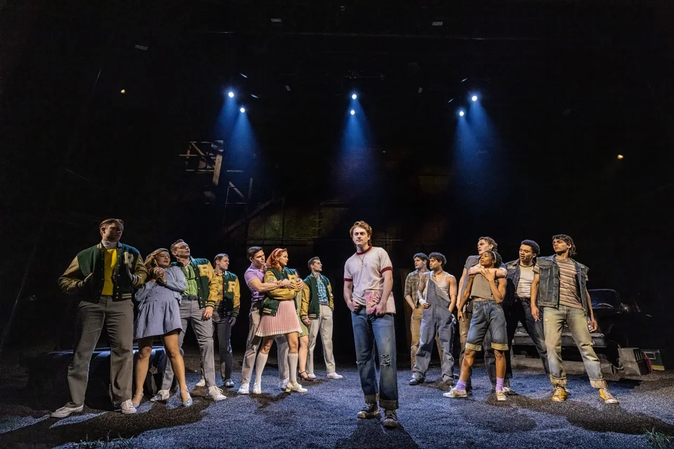 The Outsiders ensemble lined up under blue spotlights