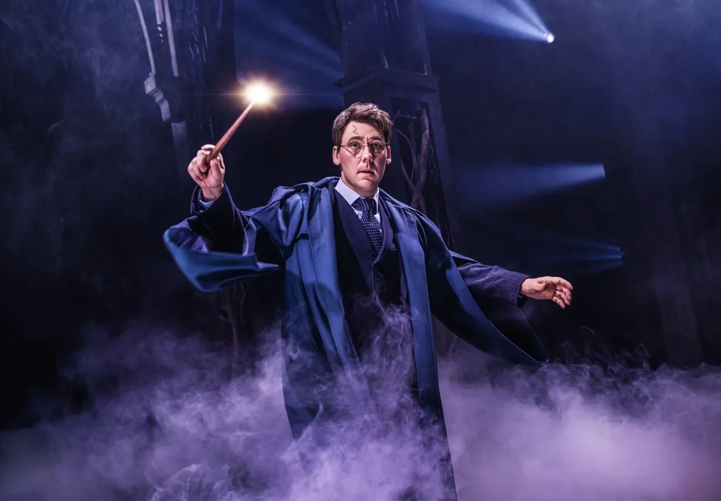 A Harry Potter and the Cursed Child performer raising a wand amid stage mist