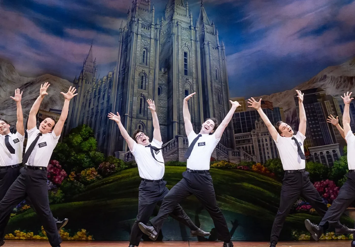 The Book of Mormon ensemble performing before a painted city backdrop